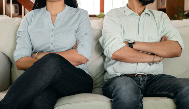 Hombre y mujer con los brazos cruzados sentados en un sofá