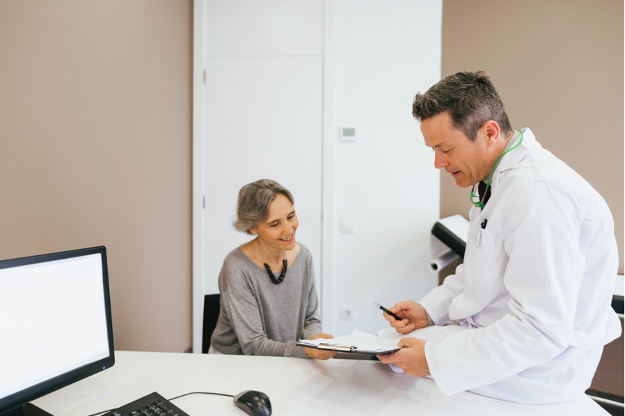 Un doctor en una consulta charla de manera informal con una paciente mientras le muestra un informe impreso en papel