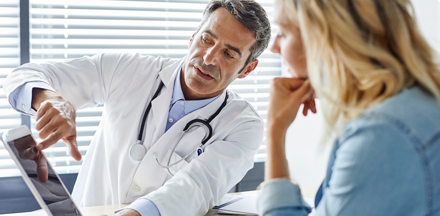 Un doctor en una consulta médica explica a una mujer un diagnóstico a través de la pantalla de una tablet